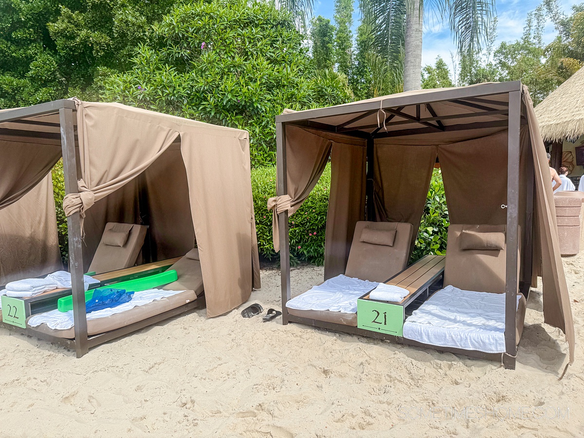Luxury day beds in the sand under a tan covering that protects the loungers from the sun and rain.