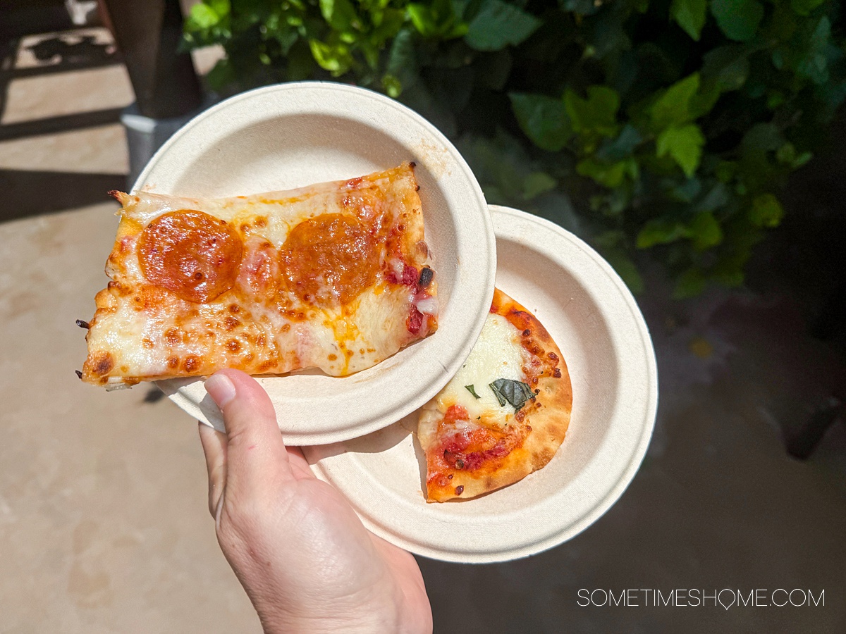 Hand holding two small plates with two small slices of pizza.