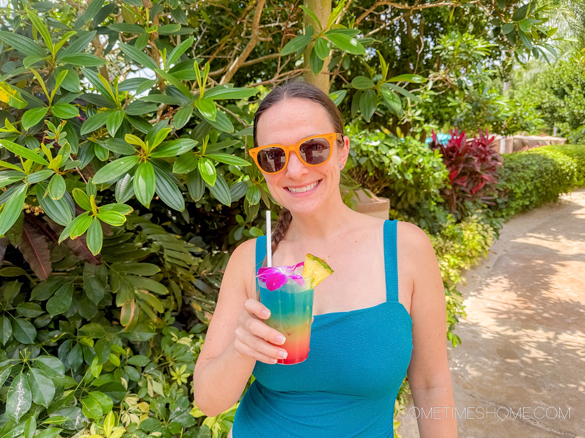 Woman wearing yellow sunglasses and a blue bathing suit holding a colorful cocktail.