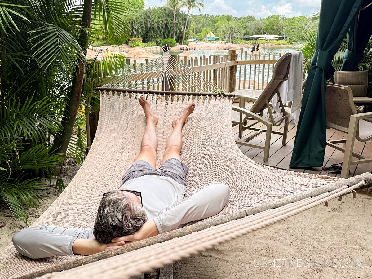 Man in a hammock with a fence and water in the distance.
