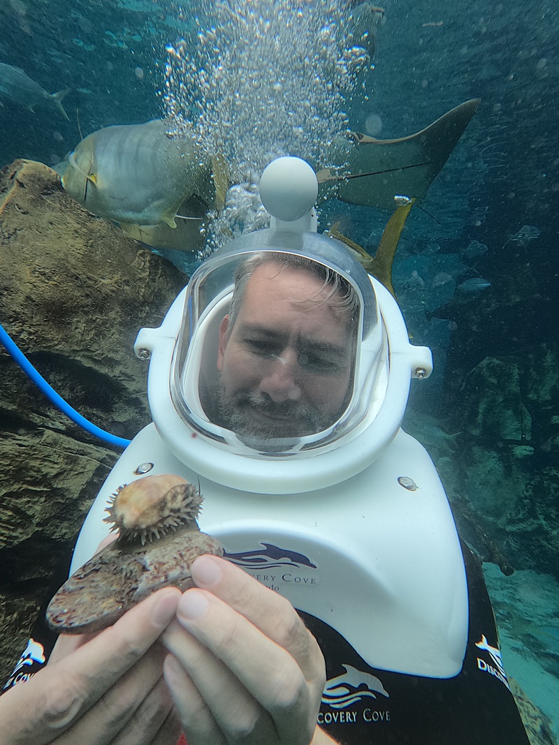 Man holding a shell in the water with a dive helmet on.