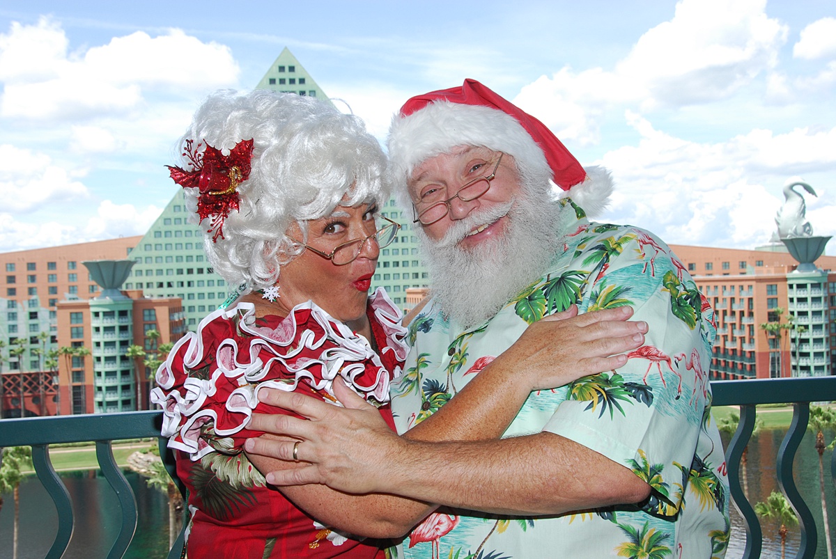 Santa and Mrs. Clause hugging in tropical attire in front of the Swan and Dolphin resort hotels.