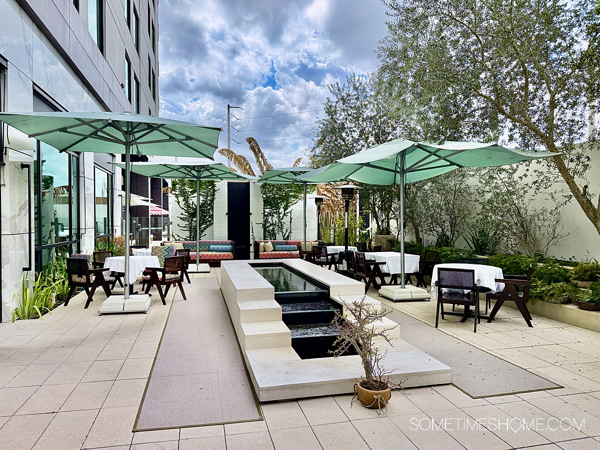 Outdoor square with a central fountain and green umbrellas over tables.