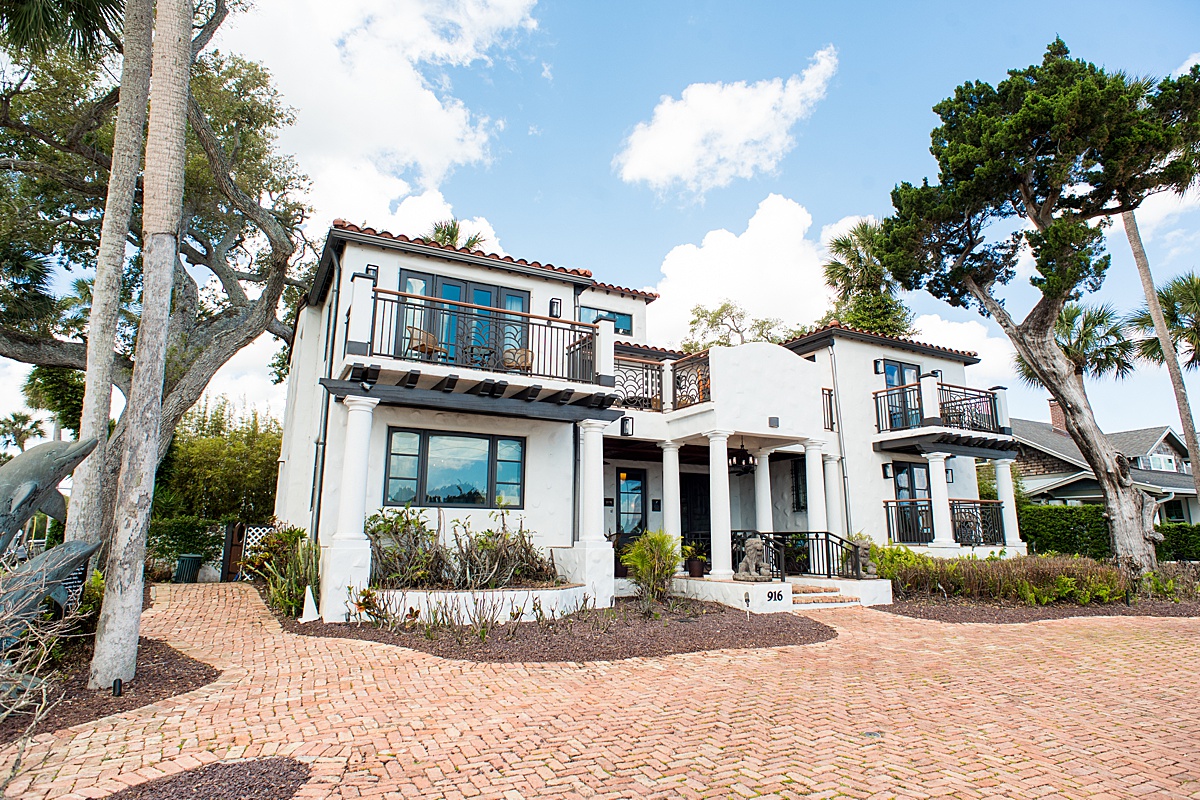 Multi-story boutique hotel with balconies, painted white with a brown brick driveway.