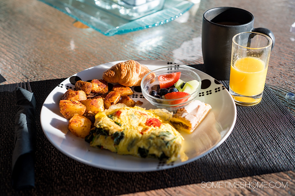 Omelet, hash brown potatoes, a croissant and fruit on a place with a small glass of orange juice next to it on a black placemat on a table.