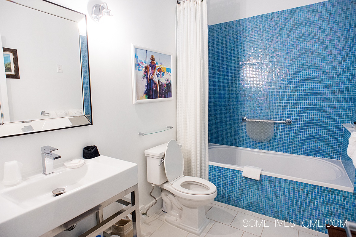 Bathroom with a blue tile wall behind the tub in the shower, a white sink basin under a mirror on the wall and a white toilet