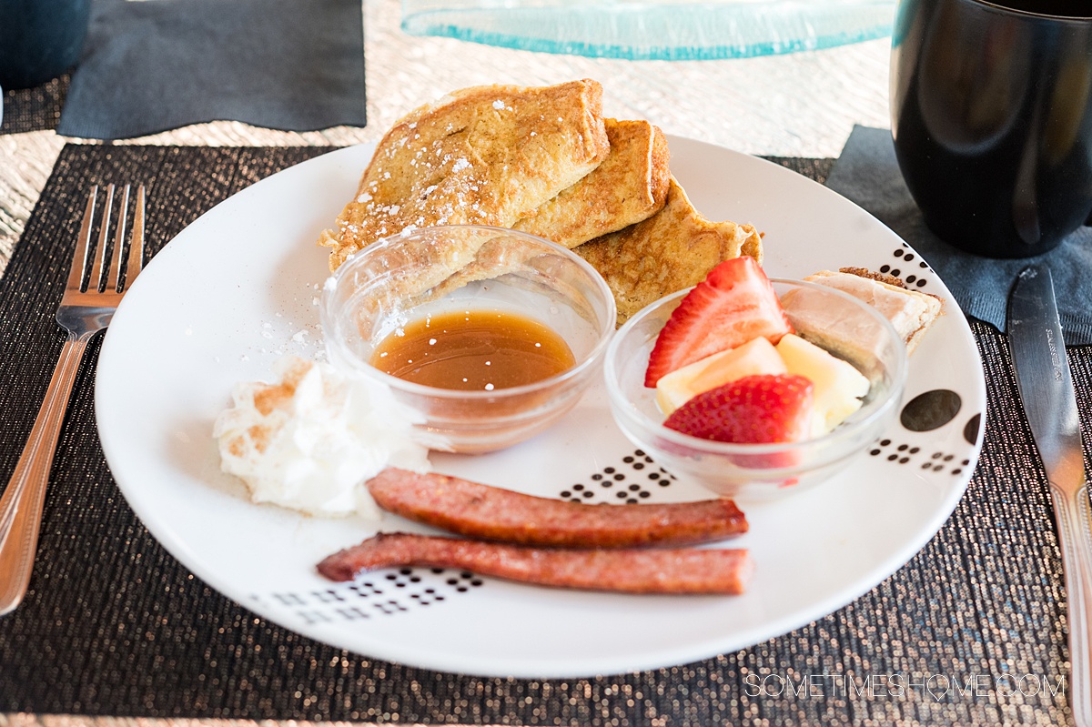 Sausage, French toast, strawberries and a small bowl of fruit on a plate.