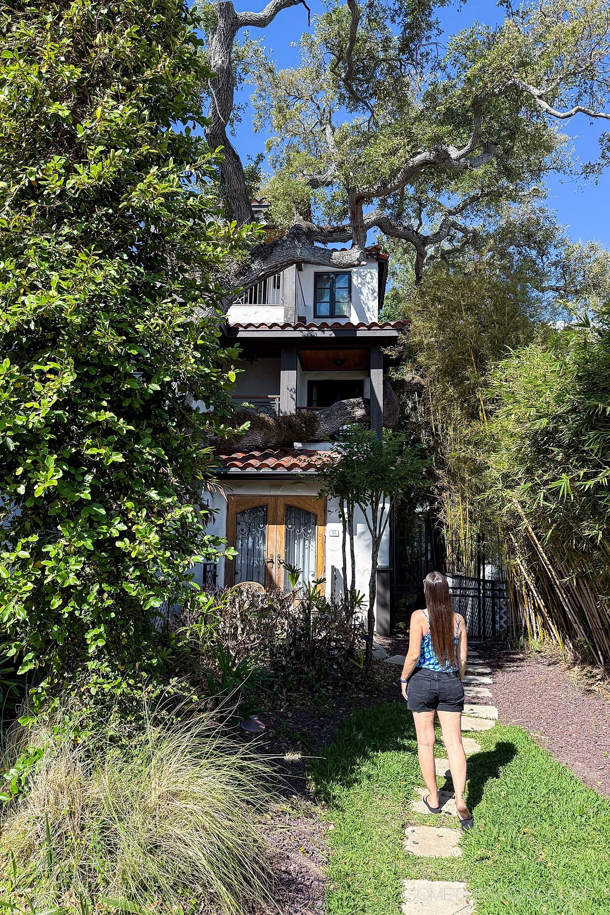The back of a woman looking up at the balcony of a boutique hotel wing in the midst of trees.