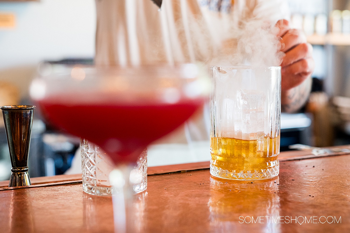 Two glasses on a bar with the one on the right with smoke coming out of it.