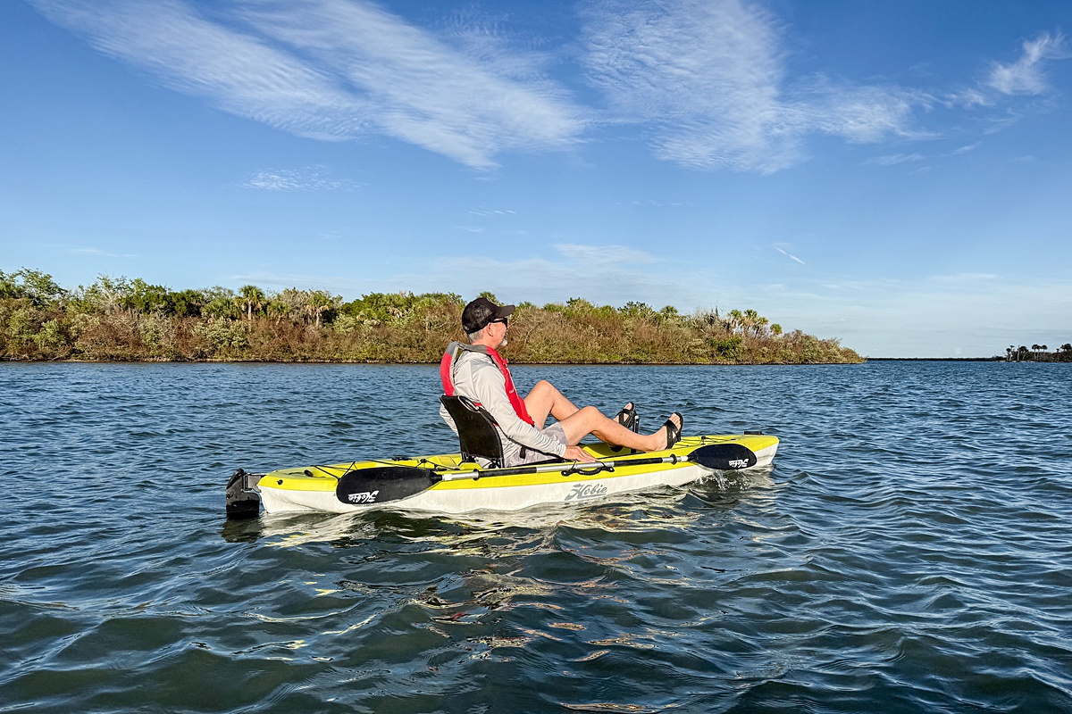Man on a neon green kayak in the water with an island filled with trees in the far distance.