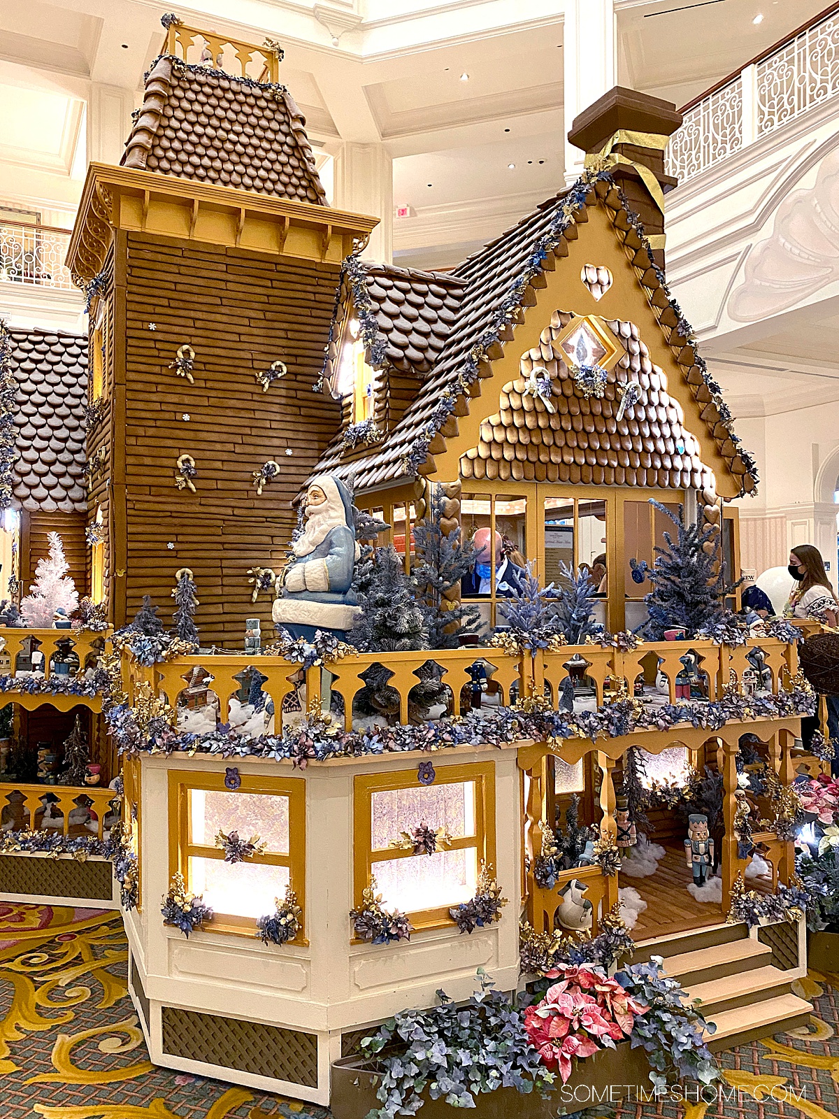 Huge gingerbread house illuminated with lights and purple flowers.